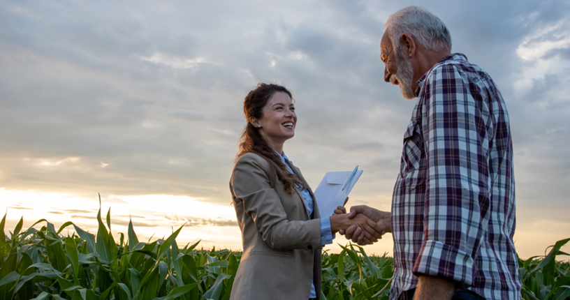 Agricultor y mujer de negocios dándose la mano en un campo